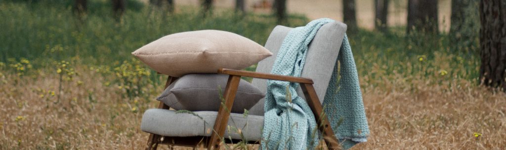 Cojines decorativos sobre una silla con una manta, en un entorno natural: un ejemplo de estilo y conservación para quienes buscan consejos sobre cómo cuidar sus cojines.