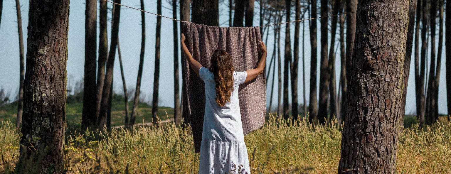 Mulher a estender têxteis naturais ao ar livre — durabilidade e cuidado fácil dos têxteis naturais para um sono melhor